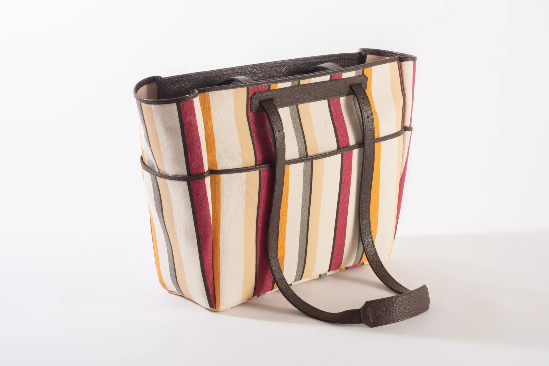 Vista laterale della borsa Liber_TO di Lemanì, mostrando la fantasia multiriga e gli spallacci in pelle marrone scuro, su sfondo bianco. La borsa Lemanì Liber_TO combina un design accattivante con la praticità, ideale per l'uso quotidiano e le passeggiate.